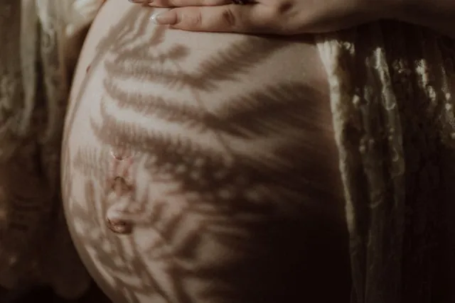 A hand resting on a pregnant belly in warm light